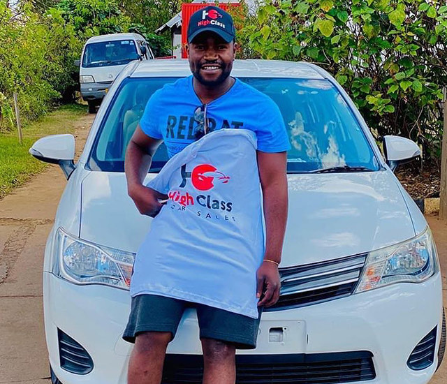 A customer holding up a branded shirt in front of his white Toyota